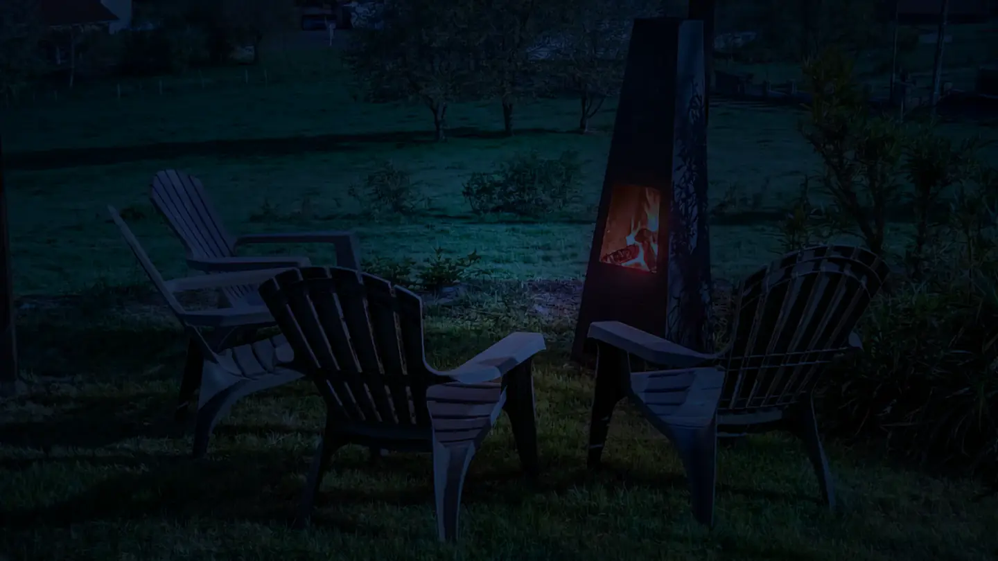 Cheminée extérieure et fauteuils de jardin à l’Ancienne École après la tombée de la nuit.