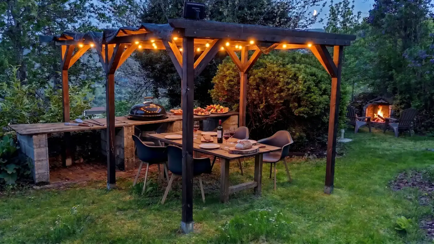 Cuisine et espace repas couverts dans le jardin de l’Ancienne École au crépuscule.