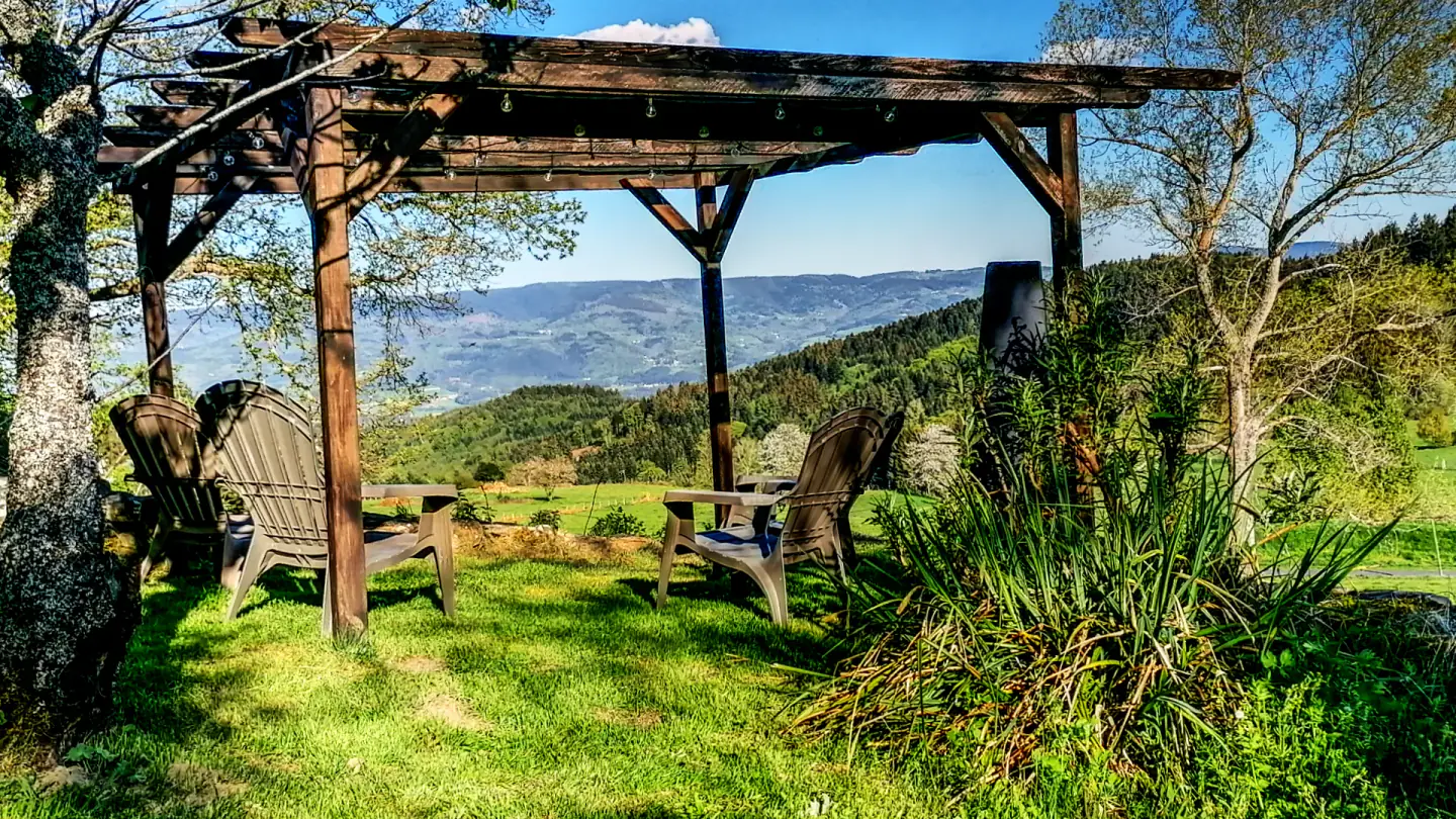 Pergola en bois du jardin de l’Ancienne École face aux collines et aux prairies.