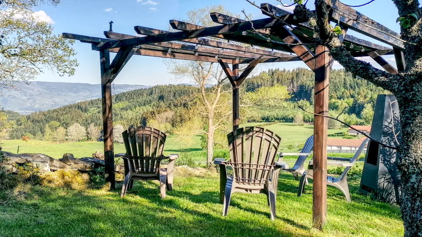 Fauteuils sous la pergola de l’Ancienne École face à la campagne du Livradois-Forez.