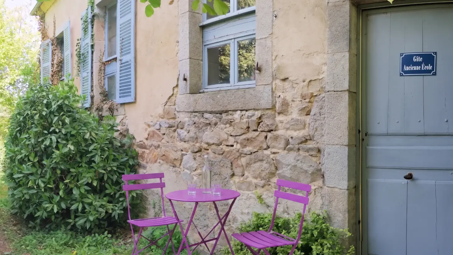 Entrée en pierre de l’Ancienne École avec volets bleus et table bistrot.